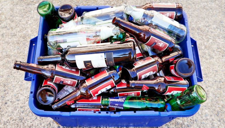 Wine and beer bottles fill a blue recycling bin