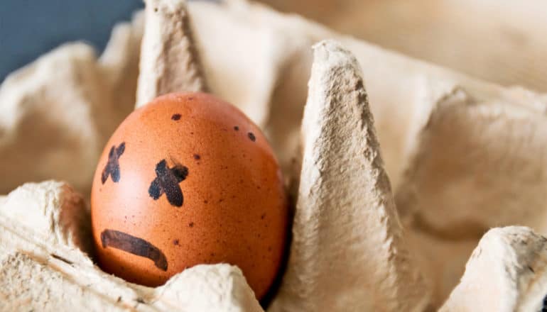 A single brown egg sits in the container with a frowning face and X's for eyes