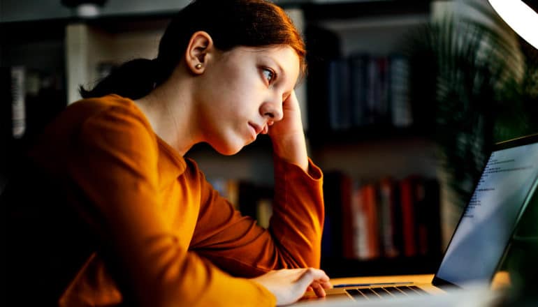 A college student leans on her hand while staring at a computer screen