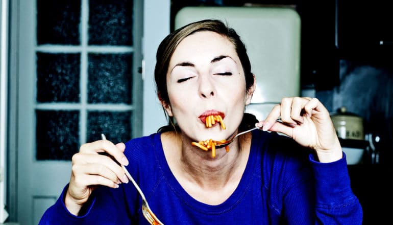 A woman closes her eyes while eating spaghetti with red sauce in her kitchen alone