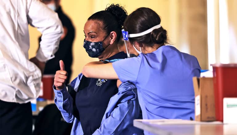 A woman gives a thumbs up while getting the new COVID-19 vaccine