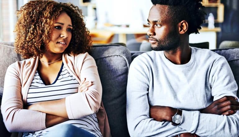 A couple sits on the couch with their arms folded while arguing