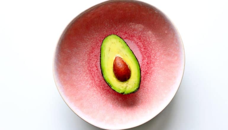 An avocado sits in a pink bowl on a white background