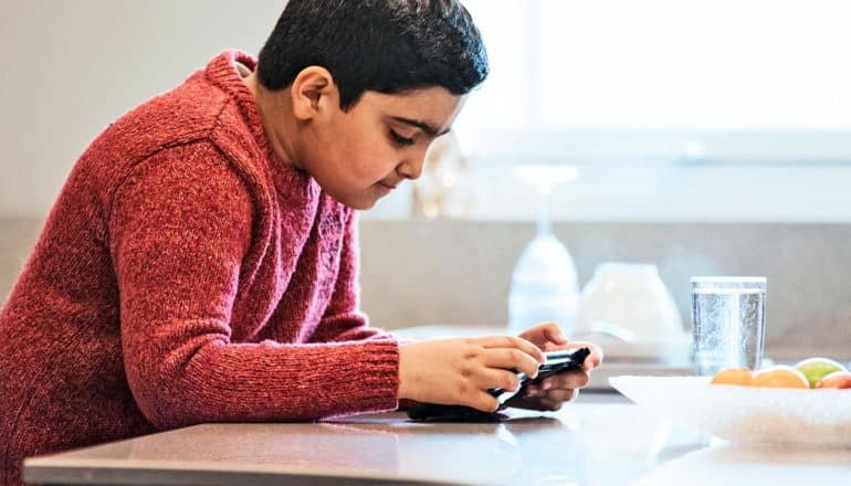 A young boy looks down at a screen while he plays a game