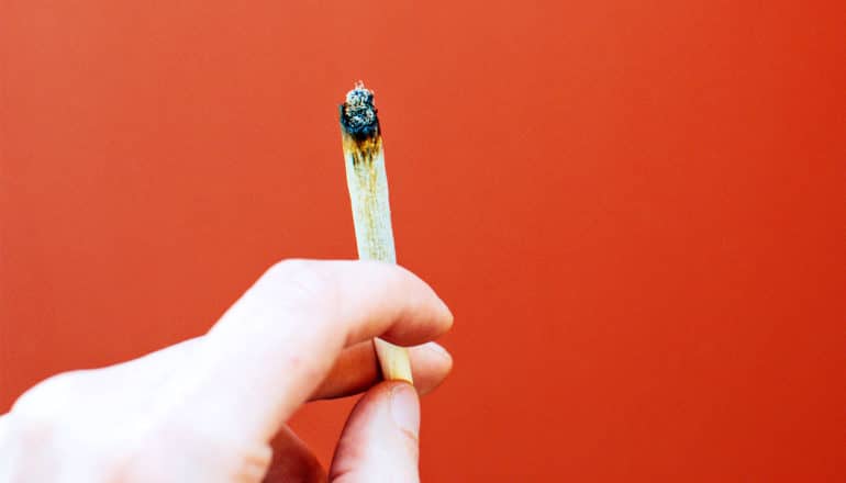 A man holds a joint against an orange background