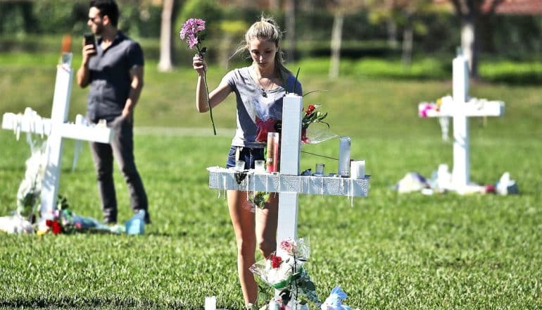 A young woman walks up to a grave or memorial in the shape of a cross with flowers