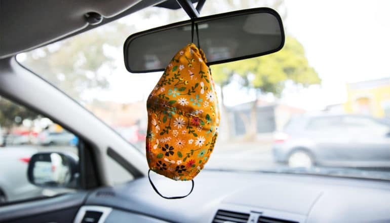 A floral patterned face mask hangs from a rear view mirror