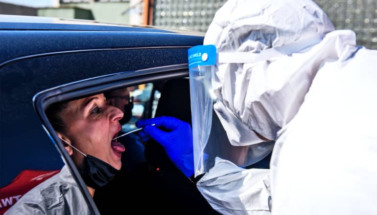 A woman opens her mouth and a person in PPE swabs her cheek