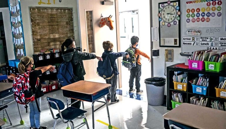 Kids line up to leave their classroom, holding their arms out in front of them to make sure they stay socially distanced