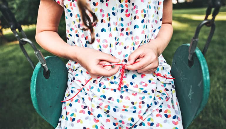 A young girl makes a friendship bracelet while sitting on a swing