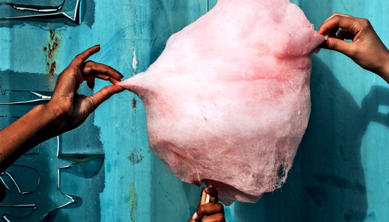 People pick at pink cotton candy against a blue wall