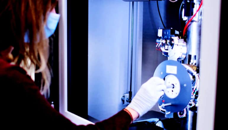 A research puts a sample into a machine behind glass