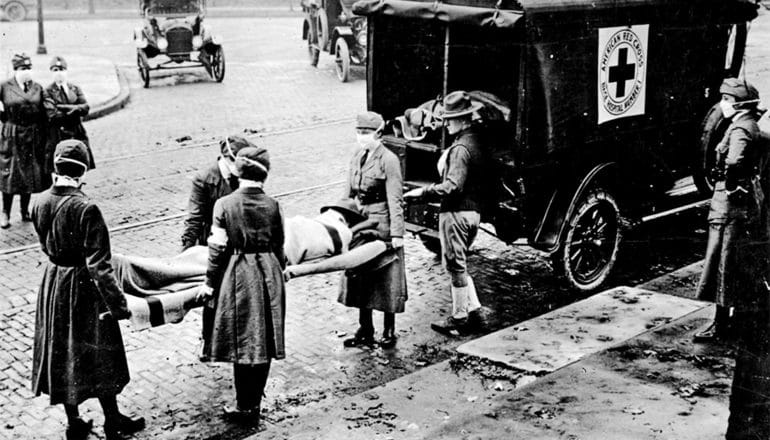 Medical workers lift a person on a stretcher into the back of an ambulance