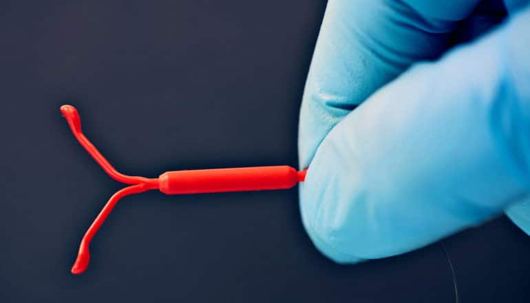 gloved hand holds red IUD