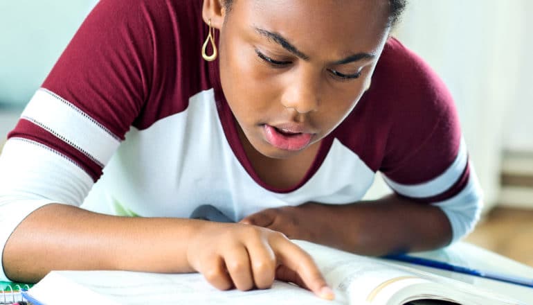 A young student reads a text book, following with her finger