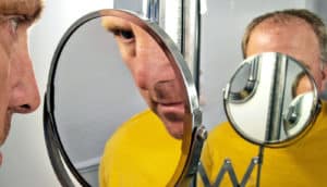 A man looks in a mirror with another covering his face