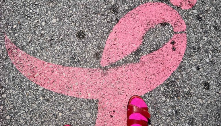 A pink ribbon painted on concrete with a person's pink shoe and sock in the frame