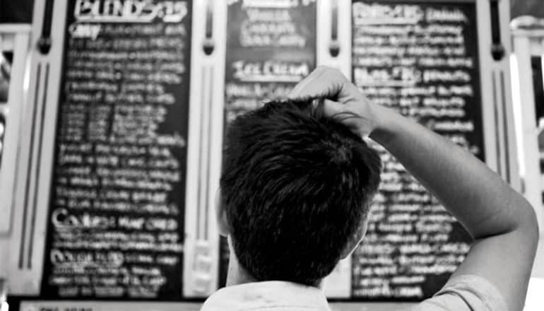 A man looks up at a huge menu and grabs the hair on the top of his head