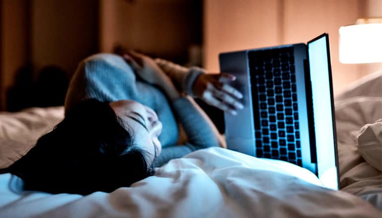 A woman lies on her side in bed looking at her laptop