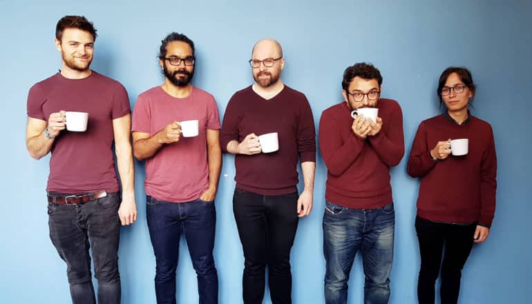 diverse group of 5 adults in maroon tops, jeans, holding white coffee cups