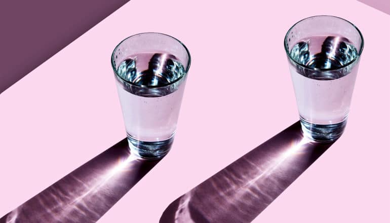 Light shines through two glasses of water on a pink surface