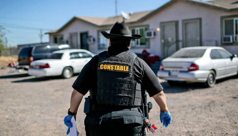 person in black garb labeled "constable" walks toward house