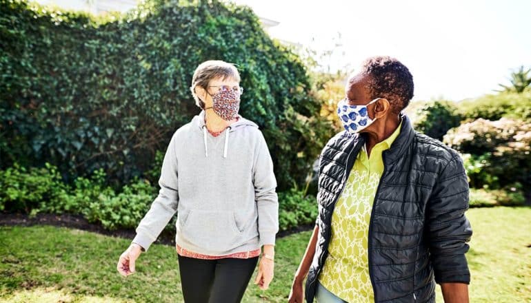 Two women walk through a park wearing face masks