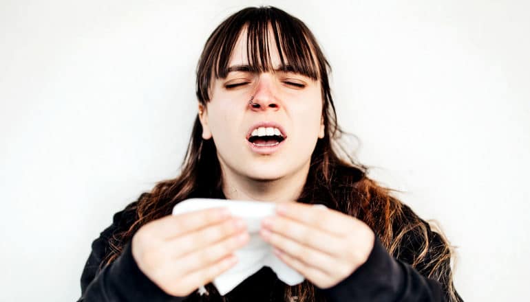 A young woman is about to sneeze into a tissue