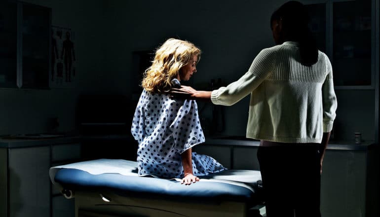 A patient sits in a doctors office with a spotlight on her