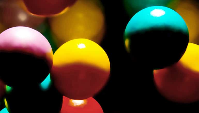 Several colorful gumballs fall in a dark space