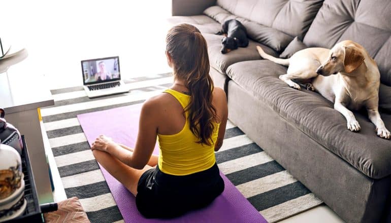 A woman meditates while sitting on the floor in front of her laptop