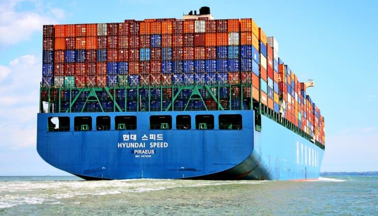 A huge container ship with many different colored shipping containers moves across the ocean