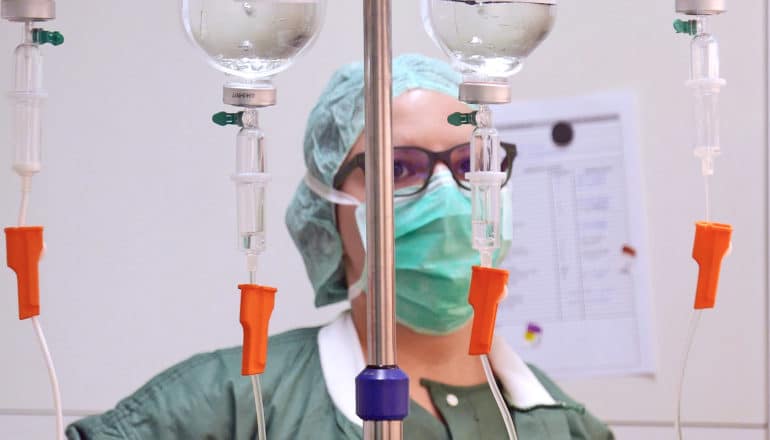 medical staff in mask stands behind four drips on IV pole