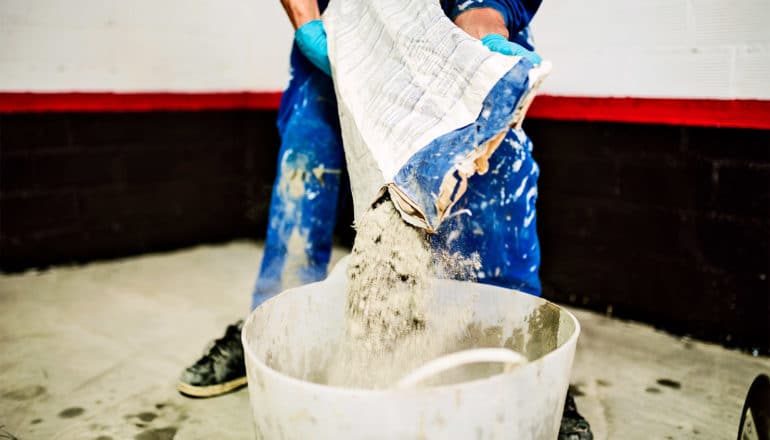 A person pours dry cement mixture into a bucket