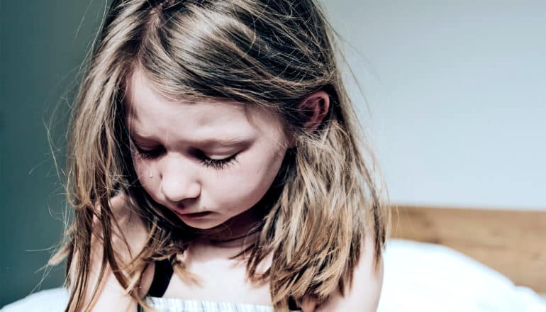 A young girl cries while sitting alone on her bed