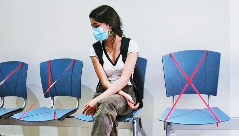 A young woman sits in a hospital waiting room with the chairs around her taped off for social distancing