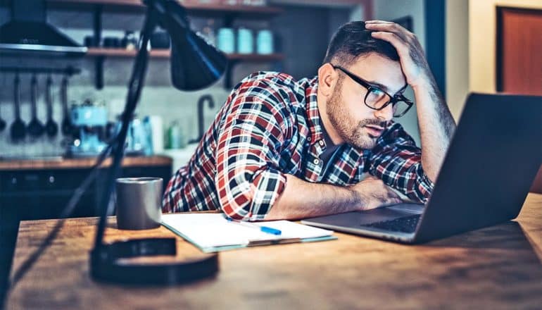 A man leans on his desk while on a work call