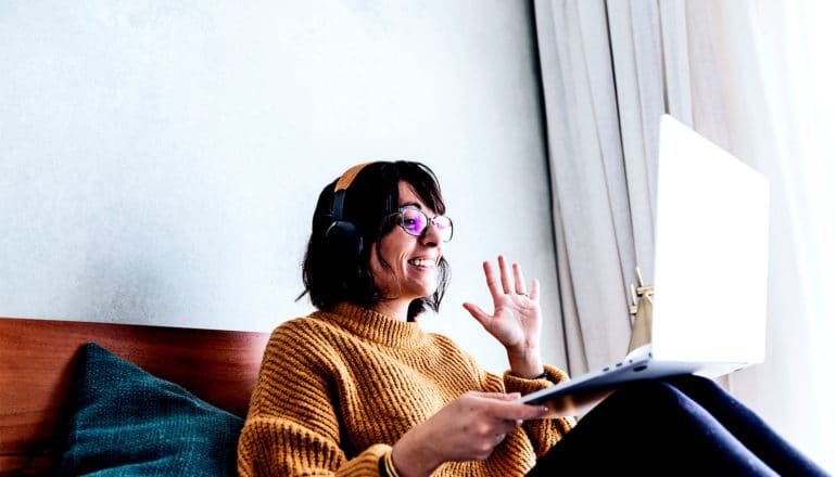 A woman waves to her laptop camera during a virtual meeting