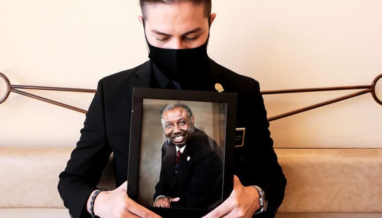 somber person holds framed photo of Black man in clerical collar