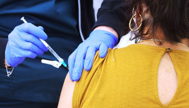 gloved hands use syringe on arm of person facing away from camera