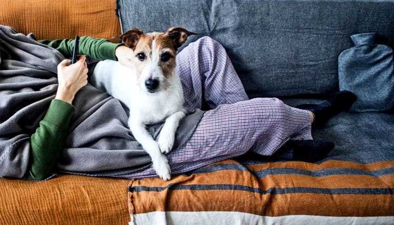 A woman feeling ill on the couch with a dog on her lap