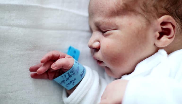 A baby with a blue hospital bracelet on a white blanket