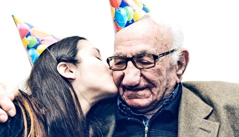 A young woman kisses her grandfather, both wearing party hats, on the cheek