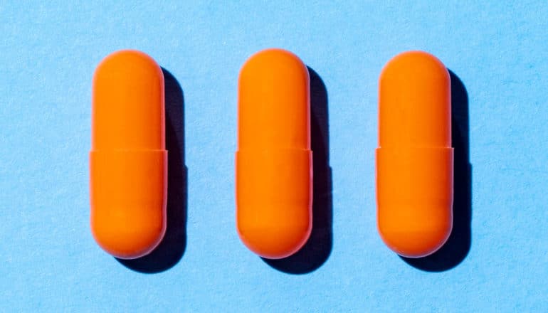 Three orange pills on a blue background