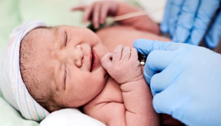 A health care worker wearing blue gloves checks a newborns heartbeat