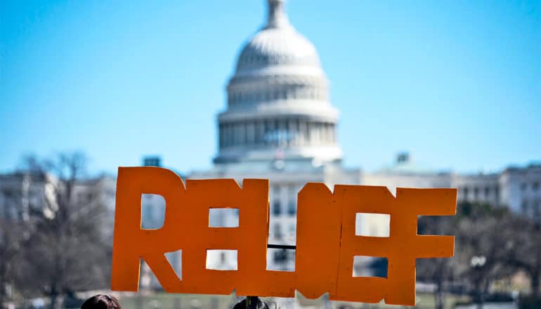 A protestor holds a sign that reads "Relief" in front of the US Capitol building