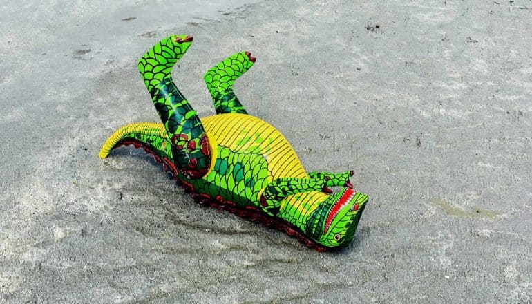 A green dinosaur toy lays on its back in the dirt