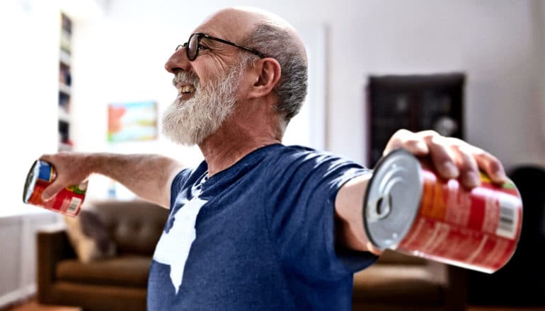 A man lifts two large cans of soup while smiling