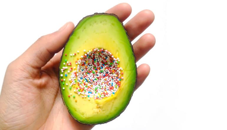 hand holds avocado with sprinkles