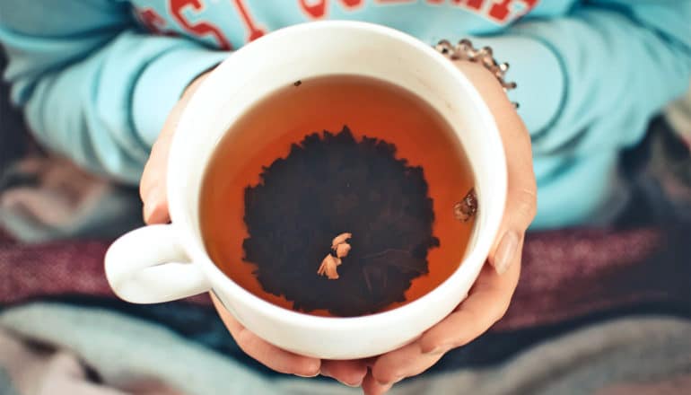 A person holds a white mug of tea with leaves at the bottom